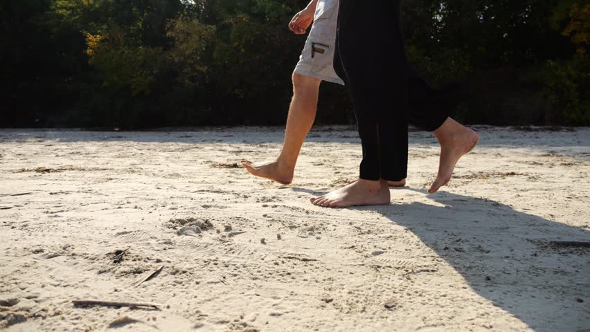 Male and female legs of pair walking on sandy beach. Bare feet of couple stepping along sand shore at sunny day. Lovers spending time together at resort. Concept of summer vacation or holiday