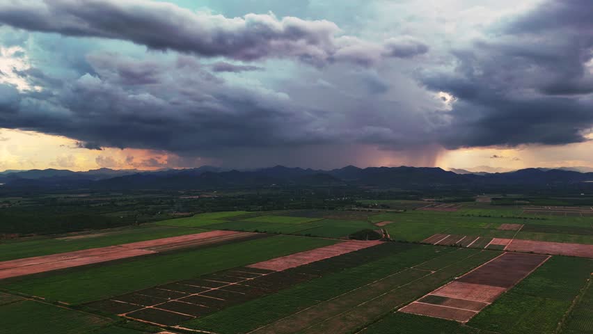 Aerial view of Storm clouds and sunset light over farmland and mountains in dramatic cinematic landscape
