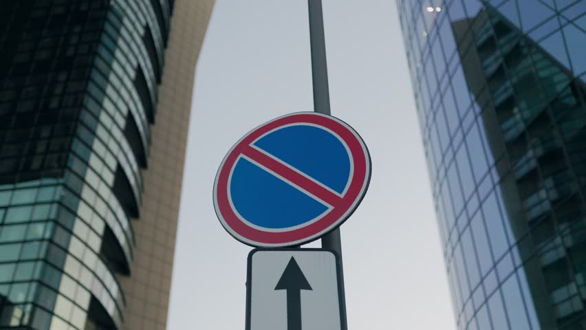 Urban traffic sign showing no parking with an upward arrow, placed among tall modern skyscrapers in the city center, symbolizing order, rules, and city life.
