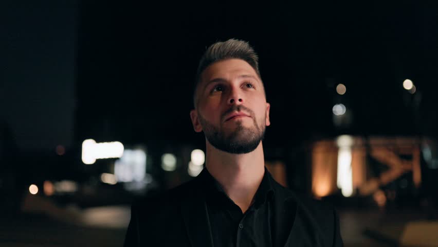 Elegant young man with a beard wearing a suit poses outdoors at night. His stylish look and confident vibe reflect both modern fashion and urban mystery.