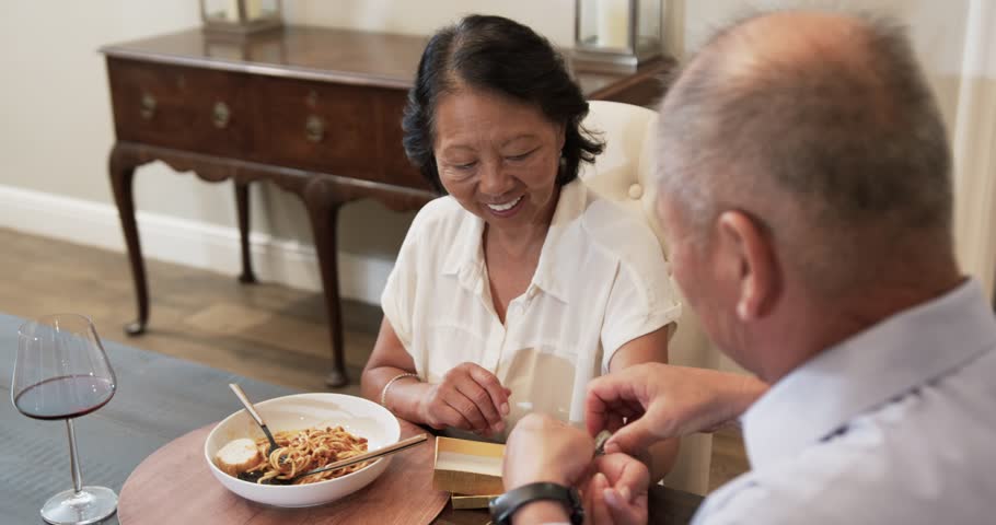 Asian senior couple enjoying pasta and wine at home, sharing laughter and conversation. dining, lifestyle, meal, togetherness, companionship, happiness