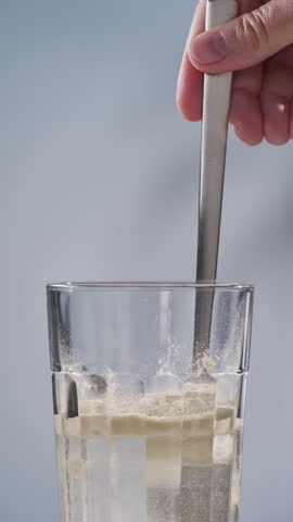 human hand mixing protein powder with water in glass.  whey sports nutrition. dry mixture for preparation of sporting or dietary drink.