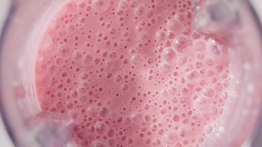 Strawberry and banana pink milkshake blended in blender with splashes. top view. slow motion. Healthy protein smoothie drink concept , food closeup. Protein powder falling in smoothie from spoon