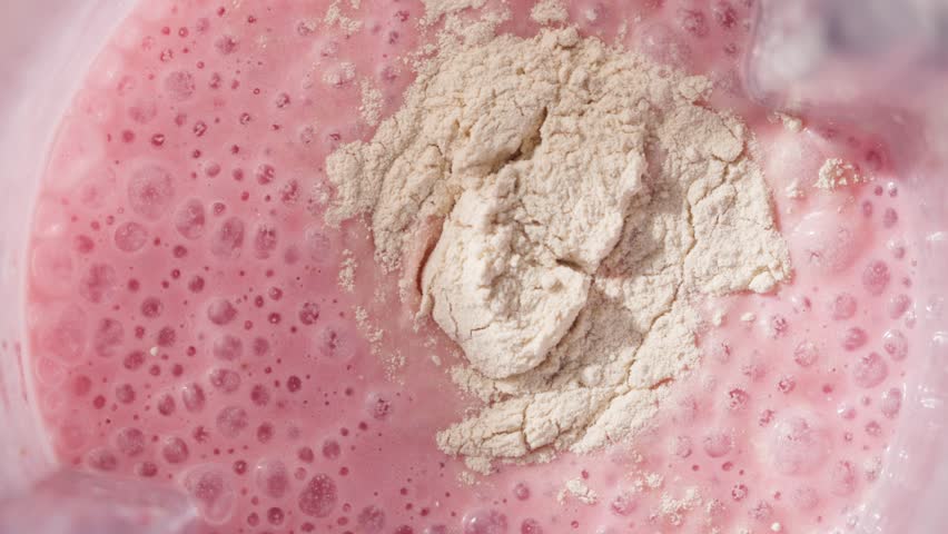 Strawberry and banana pink milkshake blended in blender with splashes. top view. slow motion. Healthy protein smoothie drink concept , food closeup. Protein powder falling in smoothie from spoon