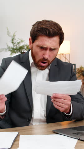 Middle-aged businessman at home office acts auditor and tosses rejected receipts into air angry about waste. Freelancer guy at table gathers bills sorts papers and plans next steps to correct records.