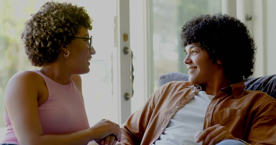Couple starting talk as woman leaning and speaking animatedly on couch by sliding door for support. Intimacy, communication, connection, candid, candidness, relaxation, natural