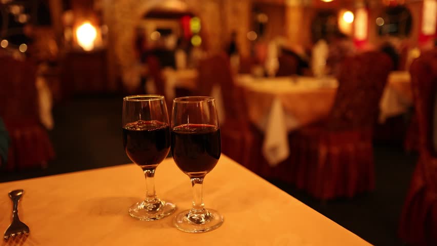 Two red wine glasses on table, warm ambient lighting, shallow focus, upscale restaurant interior