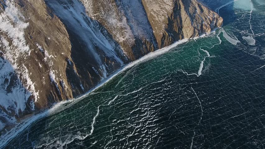 Epic helicopter view frozen Lake Baikal winter patterns. Siberia majestic coastal landscape with mountain shoreline, ice crack formations, nature reserve, northern wilderness, breathtaking phenomenon