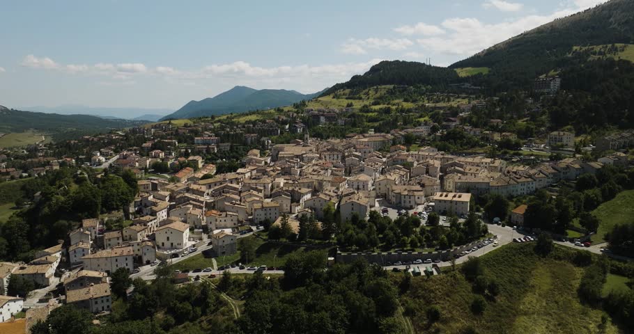 Aerial view of the charming town of Pescocostanzo nestled amidst rolling green hills and mountains, showcasing a beautiful contrast of nature and architecture, Italy.
