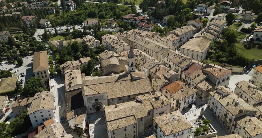 Aerial view of buildings and a church with tiled roofs, streets, and green trees providing a contrast to the structures, Pescocostanzo, Abruzzo, Italy.