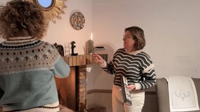 Two middle-aged women lighting a candle together by the fireplace on a cozy winter day - Powered by Shutterstock - Get 15% off with code: PIKWIZARD15