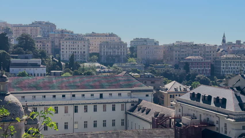A wide, panoramic view of the city of Genoa, Italy, with historic buildings, lush greenery, and the blue sea on a bright, sunny day. High quality 4k footage