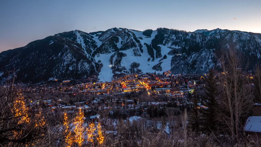 Timelapse of Aspen, Colorado at sunset with glowing city lights beneath snow-capped Rocky Mountains. Stunning winter evening scenery, perfect for travel, nature, and lifestyle projects.