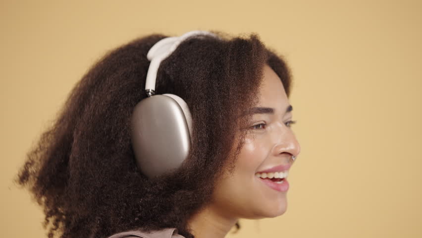 Biracial woman listening music, enjoying dance, headphones on beige backdrop - Powered by Shutterstock - Get 15% off with code: PIKWIZARD15
