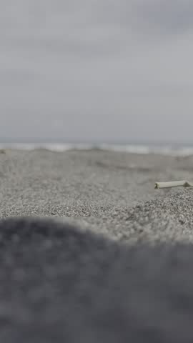 This is a short, static video shot from a very low angle on a gray sand beach. The immediate foreground is out of focus, drawing attention to the textured sand in the middle of the frame. In the blurr