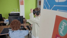 Rear view of curly schoolboy wearing denim shirt sitting by desk and working with desktop computer while his classmate in virtual reality headset watching 3d presentation - Powered by Shutterstock - Get 15% off with code: PIKWIZARD15