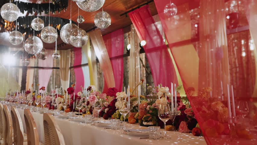 Wedding table setting in a restaurant or tent, with flowers, candles and glasses. Without food and people. Decorated dining table with red curtains and disco balls, suitable for special events and