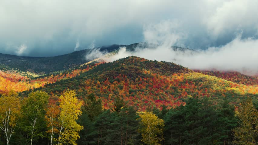 Adirondack Mountain, New York State. A vivid autumnal landscape captured during the fall season, with a mountain range shrouded in mist and clouds in the background.