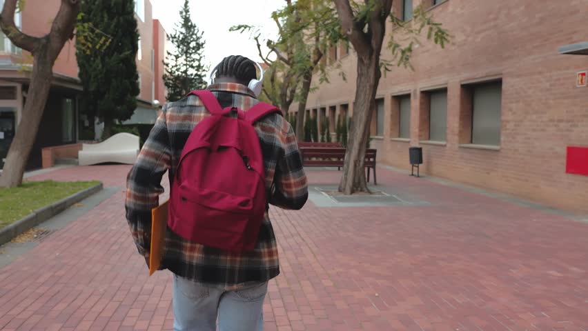 Happy student walking in university campus listening to music in slow motion. Young black student walking happily through university campus listening to music