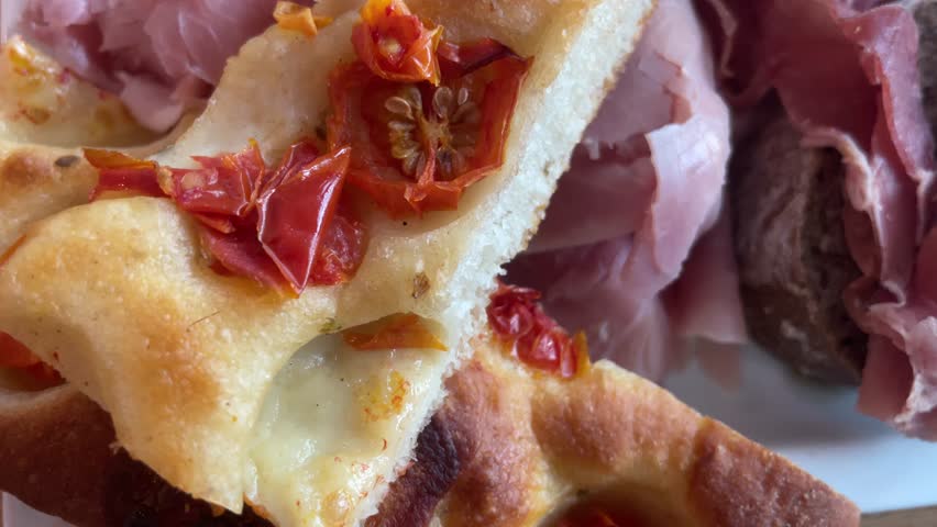 Cutting board with delicious and romantic food from the beautiful country of Italy. Amazing cured meats in 4K meet delicacy such as olives, dry tomatoes and focaccia bread.