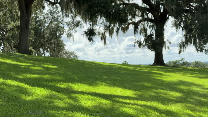 Pan right across green dappled lawn of Iron Mountain summit, part of an expansive garden sanctuary in central Florida, to scenic view of expansive surrounding area on a sunny morning in summer
