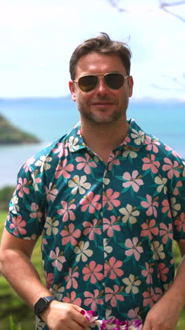 a man in a Hawaiian national shirt wears a necklace with a wreath of flowers around his neck. A happy male tourist holds the national Hawaiian orchid and hibiscus necklace as a token of welcome