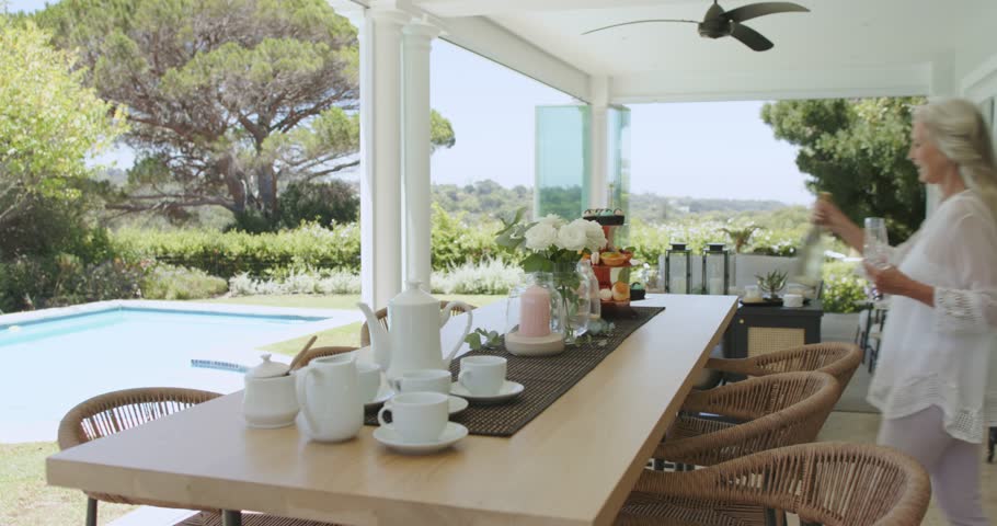 Diverse female friends responding to sunshine, serving petit fours, pouring juice on patio by pool. Friendship, outdoor, leisure, elegance, celebration, warm, rustic