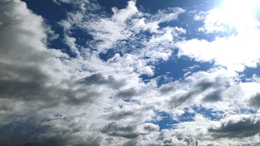 The video captures a vibrant expanse of a blue sky adorned with numerous clouds, with the sun brightly shining through, creating a classic scene of a clear to partly cloudy day.