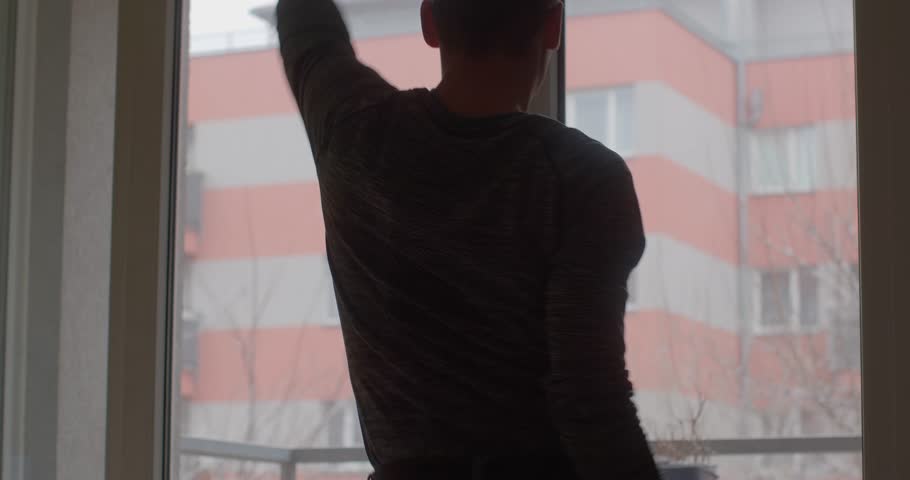 A man showcases energetic dance moves indoors, silhouetted against a bright window. Captivating expression of motion and rhythm.