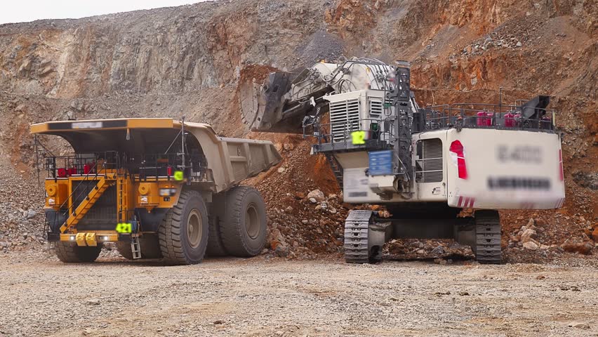Excavator loads copper ore into big dump truck in open gold pit mine. Process gold mining industry workplace.