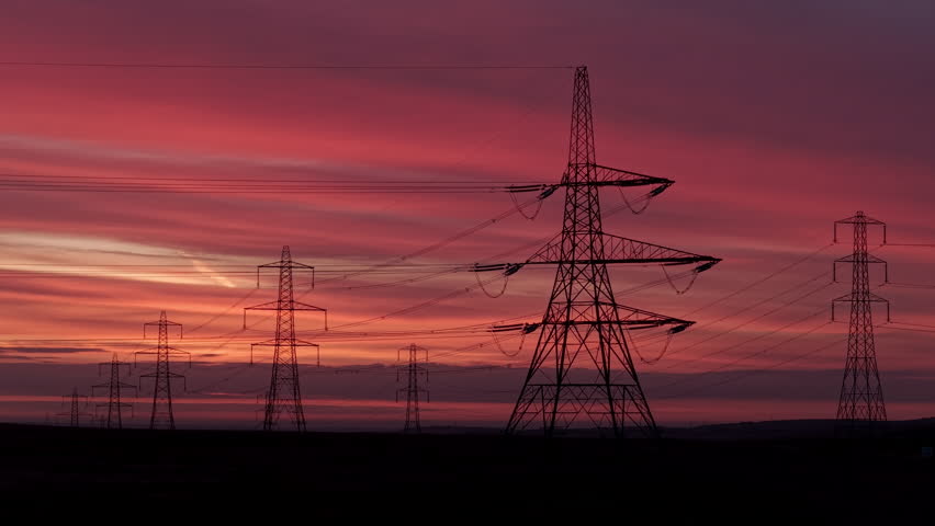 Majestic Power Transmission Pylons Silhouette Against a Vibrant Sunset Sky in a Rural Landscape