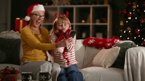 Grandmother and granddaughter wearing santa hats making funny faces while taking selfies on christmas eve - Powered by Shutterstock - Get 15% off with code: PIKWIZARD15