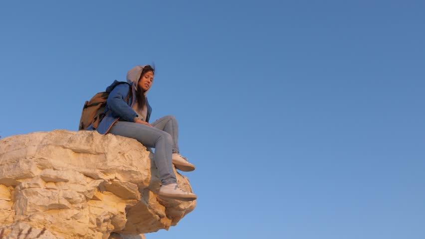 Traveler woman with backpack sits on top of mountain enjoying beautiful landscape. Free girl tourist traveler enjoys rest on top of mountain. Tourist free woman rest on rock. Travel, hiking, adventure