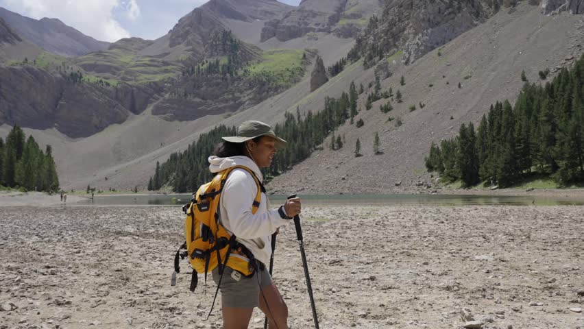 Black woman hiking in a remote mountain landscape with lake and forest, evoking Yosemite or Banff, walking with trekking gear and enjoying peaceful natural surroundings