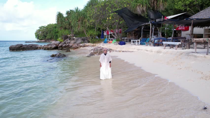 A woman in a hijab in the shallow water of a beautiful white sand beach