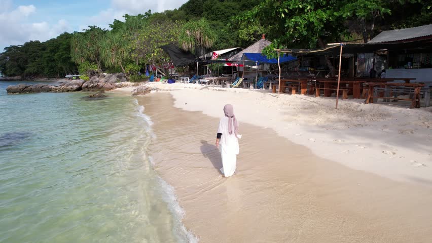 A woman in a hijab in the shallow water of a beautiful white sand beach