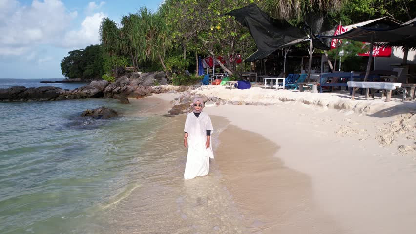 A woman in a hijab in the shallow water of a beautiful white sand beach
