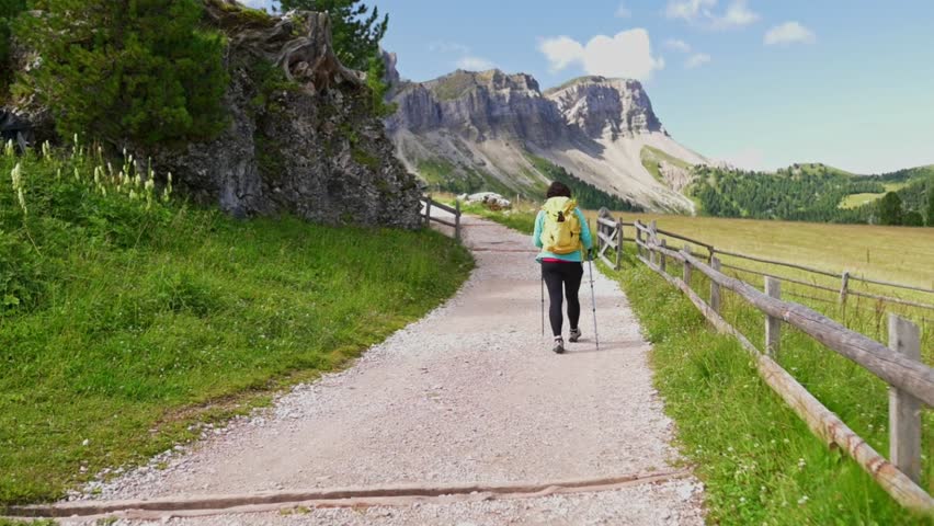 Woman hiker walking along gravel trail with Dolomites mountains in background, Italy