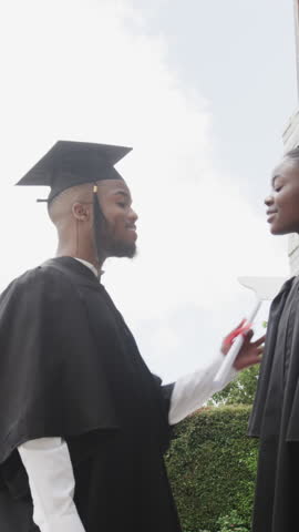 Vertical video: African American grads exchanging diplomas on patio taking smartphone selfies. Celebration, achievement, friendship, outdoor, modern, joyful, vertical video