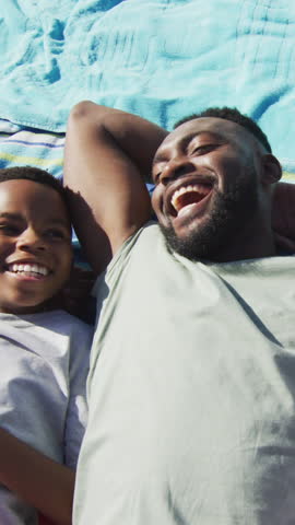 Vertical video: After dad's laugh African American dad and son laughing on picnic blanket. Families, leisure, bonding, outdoor, serenity, candid, vertical video