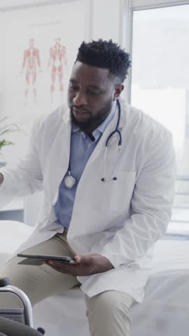 Vertical video: African American male doctor catching dumbbell entering office after tapping tablet. Medical, healthcare, professional, technology, communication, wellness, vertical video