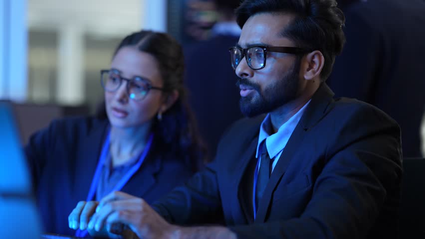 A group of female IT professionals discusses a project in their tech office. They are analyzing data and reviewing code, working as a team to solve a complex problem after hours.