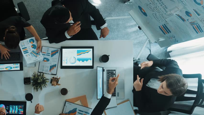 Top down aerial view of smart manager pointing at financial graph on whiteboard while diverse business team explain and plan marketing idea at meeting table with stock market statistic. Directorate. - Powered by Shutterstock - Get 15% off with code: PIKWIZARD15