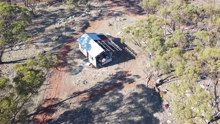 A drone flyover of a disued falling down early Australian farm building in a dry field the roof is missing animals have moved in for shelter 