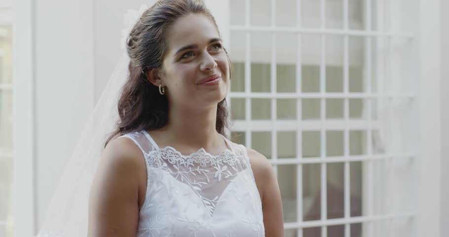 Closing eyes, bride in lace wedding dress unfolding vow card, reading vows with tears in courtyard. Romantic, elegance, celebration, femininity, serenity, joy, proposal