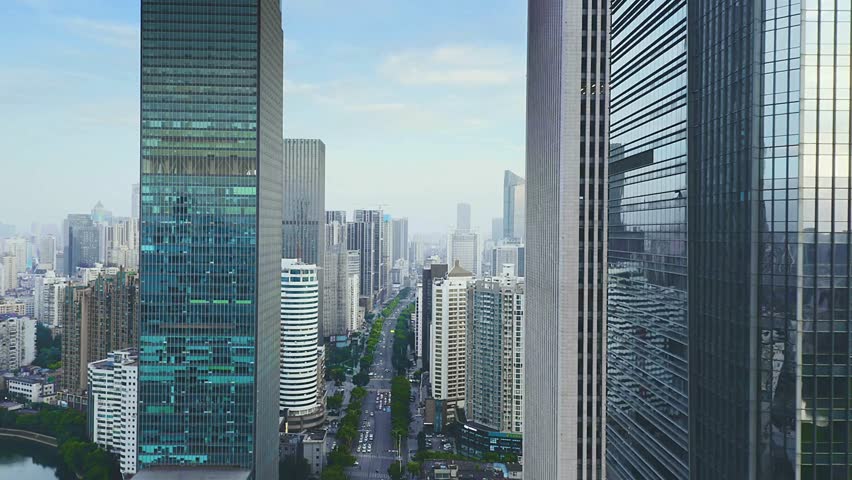 ​A cinematic drone shot flies forward between two glass skyscrapers, revealing a stunning panoramic view of a dense, modern metropolis and its sprawling urban canyon.