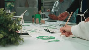 A diverse team engages in a sustainability project with eco-friendly visuals and wind turbine model. They collaborate in a modern office, focusing on innovative strategies. SACTR - Powered by Shutterstock - Get 15% off with code: PIKWIZARD15