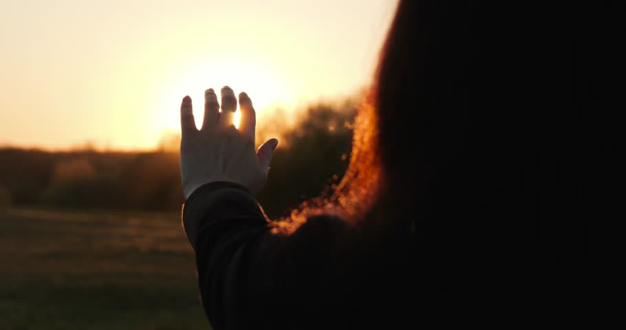 Dreaming girl raises hand to sunlight in park. Dreaming girl silhouette shows freedom and inspiration at golden hour. Warm rays and sky glow create hopeful atmosphere. Dream girl reflects aspiration.