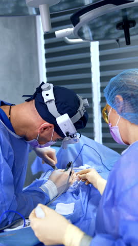 Experienced male surgeon carries out breast implantation surgery. Female nurse assists at the bust enlargement operation. Vertical video.