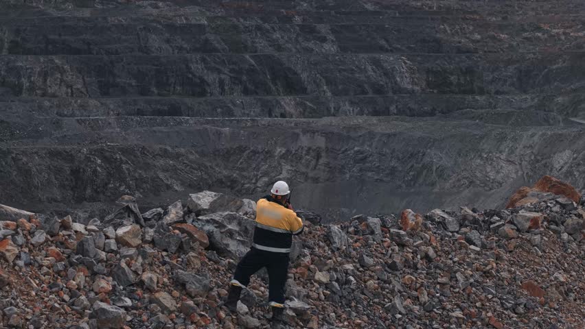 Surveying engineer controls excavator via radio on open pit mine. Process gold and copper ore mining industry workplace in quarry.